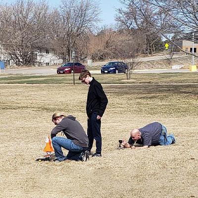 a team readies their rocket for launch while a man lays on the ground setting up a camera